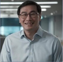 Man wearing glasses and light blue shirt smiling in office setting.