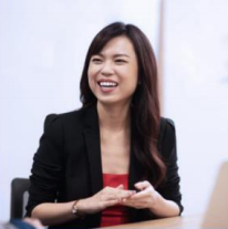 A woman in a black blazer smiles while sitting at a table.