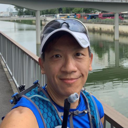 Smiling person in a blue shirt and cap by a riverside walkway.