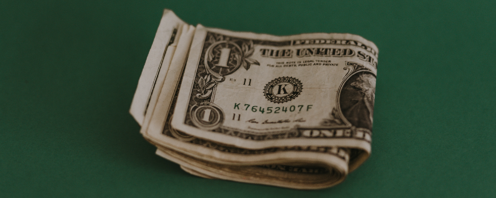A pile of one hundred dollar bills on a green surface, highlighting the financial considerations in selecting between contract vs permanent jobs