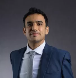 Man in a blue suit with a gray tie against a dark background.