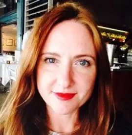 Close-up of a woman with long red hair and red lipstick in a restaurant.