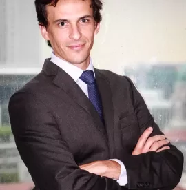 Man in a suit standing with arms crossed in front of a window.
