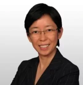 Person with short dark hair and glasses, smiling in a dark pinstripe suit.