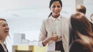 Business meeting with a woman leading a discussion, colleagues smiling and interacting.