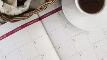 Open calendar with a coffee and bread basket on a table.