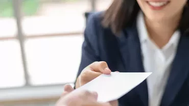 Person handing over a business card in an office setting.
