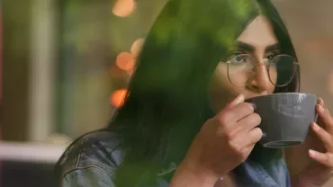 Person with glasses enjoying a hot drink in a serene setting.