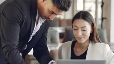 Two colleagues discussing work at a laptop in an office.