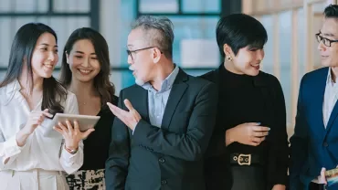 A group of five professionals in business attire having a discussion in an office setting.