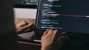 Person typing code on a laptop in a dimly lit room