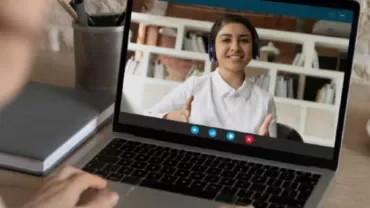 Person on a video call, smiling and giving thumbs up on a laptop screen.