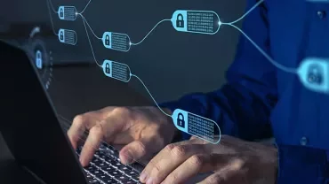 Person typing on laptop with digital blockchain graphics in the foreground.