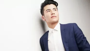 Man in a blue suit looking upwards against a white background.