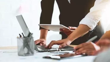 People collaborating around a table with laptops and tablets.