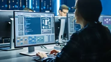 Person working at a computer with multiple screens displaying code and data diagrams.