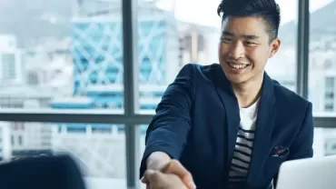 Smiling man in a suit shakes hands at a meeting in modern office.