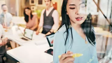 Woman writing on glass board during meeting.