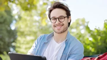 Man with glasses smiling while using a tablet outdoors