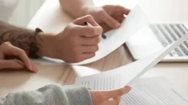 Two people working with documents at a desk near a laptop.