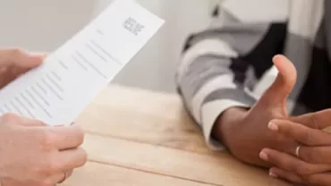 Close-up of a job interview with resume and gesturing hands at a table.