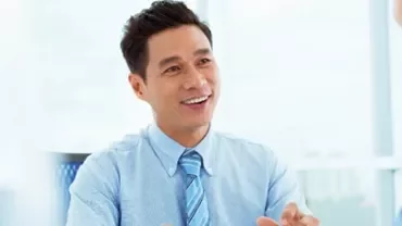Smiling man in a business meeting, wearing a blue shirt and tie.