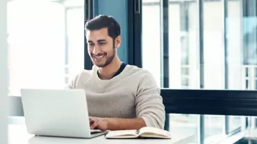 Man smiling at a laptop in a bright office.