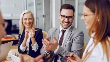 Business meeting with four people clapping and smiling.