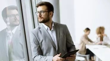 Businessman with a tablet, standing by a window, looking outside.