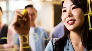 Woman writing on a glass board during a team brainstorming session.