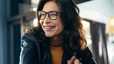 Woman in glasses smiling indoors with warm lighting.
