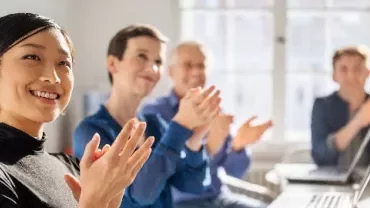 Four people sitting in a bright room, clapping and smiling.