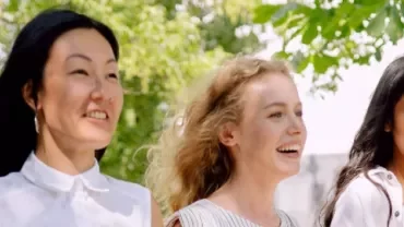 Three women walking outdoors, smiling in a sunny park.