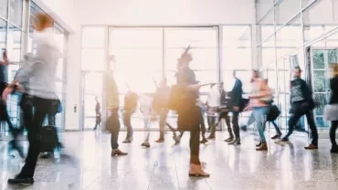 Blurred motion of people walking in a bright, spacious lobby.
