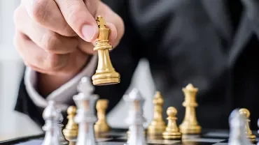 An image of a hand playing a gold-colored chess pawn.
