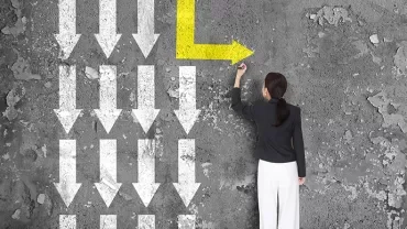 An image of a person standing facing a wall pointing at a yellow arrow to the left against white arrows pointing downwards