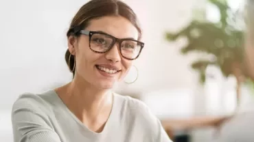 A female candidate wearing glasses smiling as she answers secretary job interview questions.