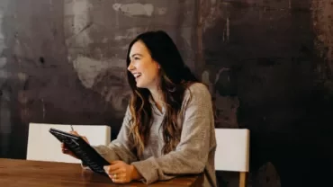 A female Personal Assistant smiling cheerfully while holding a smart tablet.