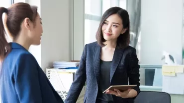 Two professional ladies having a conversation in an office room about succeeding as an office manager.