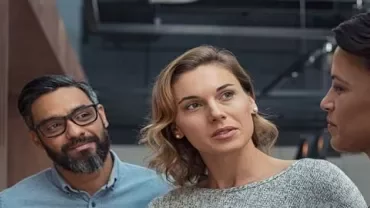 Three individuals engaged in discussion while examining a whiteboard filled with notes and diagrams.