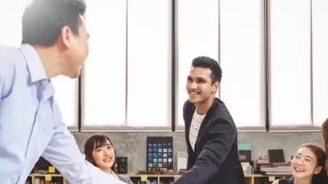 A group of professionals shaking hands in an office setting, symbolising collaboration and agreement.