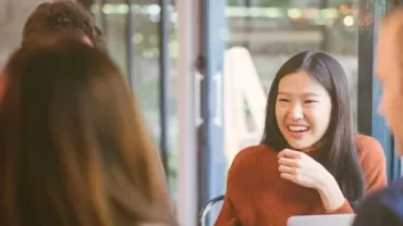A table of people engaged in conversation, highlighted by a smiling woman among them.