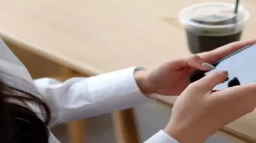 A woman sitting at a table, focused on her cell phone, with a relaxed expression on her face.