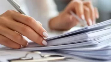 A person writing on a piece of paper with a pen, focused on their task.