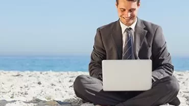 Man in a suit working on laptop at the beach.