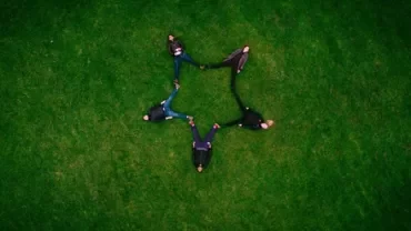 Five people lying on grass, forming a star shape with their bodies.