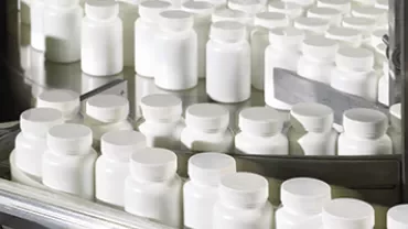 Conveyor belt with rows of white plastic pill bottles.