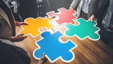 People holding colorful puzzle pieces together on a table.