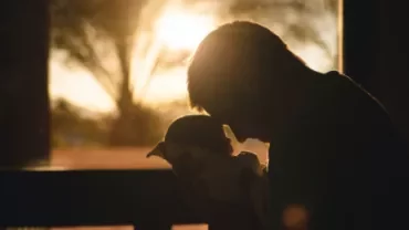 Silhouette of a parent holding a baby against sunset light.