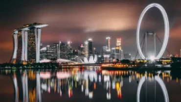 Singapore skyline at night with Marina Bay Sands and the Ferris wheel reflected in water.